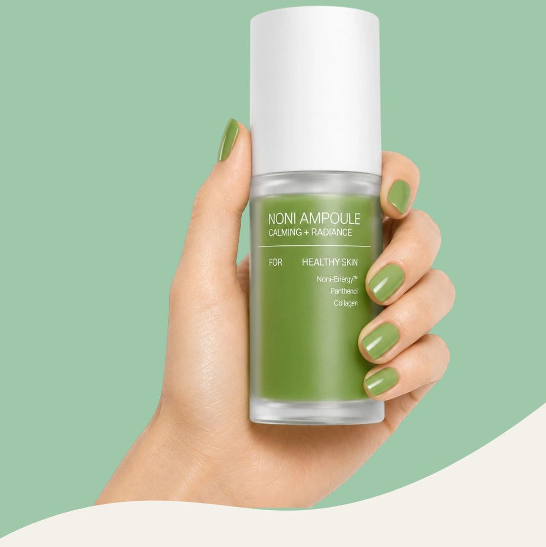 Hand holding a green skincare ampoule bottle against a light green background